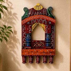 May include: A decorative wall-mounted wooden window frame featuring a vibrant hand-painted design in red, blue, green, and yellow. The structure includes an arched opening, a lattice railing, and five small hanging pegs along the bottom edge.