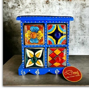 Könnte beinhalten: Ein blaues, handbemaltes Keramik-Aufbewahrungskabinett mit vier Schubladen. Jede Schublade hat ein einzigartiges, farbenfrohes Blumen- oder geometrisches Design. Das Kabinett ist mit weißen Punkten und dekorativen Akzenten verziert.