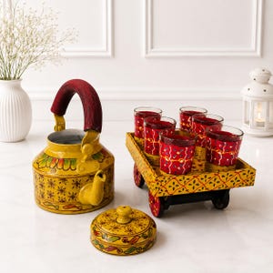 May include: A yellow metal tea kettle with a red handle and floral patterns, accompanied by a matching yellow lid and a small yellow cart on wheels holding five red glass tumblers decorated with white and green floral motifs and patterns.