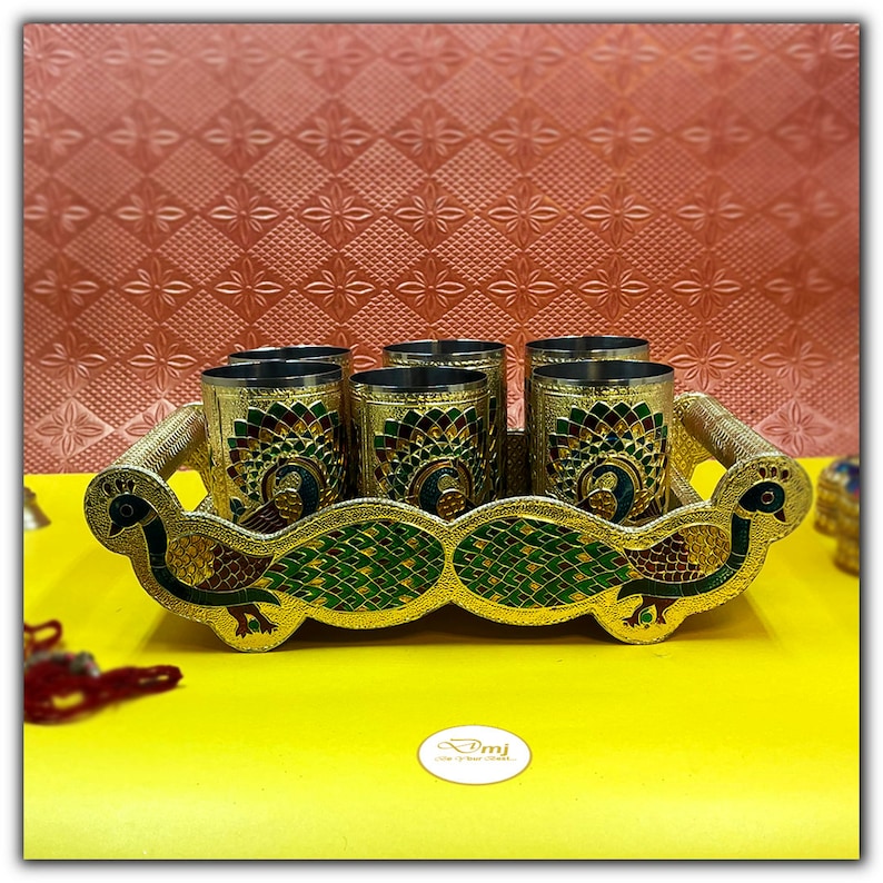 Puede incluir: Un juego de seis vasos de color dorado con dise&ntilde;os de pavo real, exhibidos en una bandeja dorada con dise&ntilde;os de pavo real. La bandeja tiene dos asas de pavo real.
