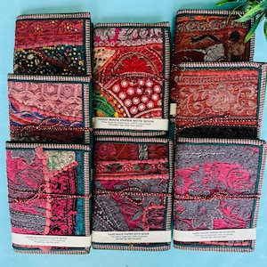 Könnte beinhalten: Eine Sammlung handgefertigter Papiernotizbücher mit farbenfrohen, strukturierten Einbänden. Die Notizbücher weisen eine Vielzahl von Mustern und Farben auf, darunter Rot, Rosa und Türkis, mit dekorativen Nähten und Verzierungen. Jedes Notizbuch ist mit einer Schnur gebunden und trägt die Aufschrift "HAND MADE PAPER NOTE BOOK".