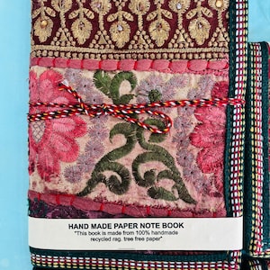 Puede incluir: Un cuaderno de papel hecho a mano con una cubierta con patrones florales bordados en tonos de rojo, rosa y verde. El cuaderno está encuadernado con un cordón colorido e incluye el texto "HAND MADE PAPER NOTE BOOK".