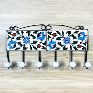 Könnte beinhalten: Ein dekorativer Wand-Kleiderhaken mit sechs Haken. Der Kleiderhaken ist aus Metall und hat ein blaues und weißes Blumenfliesenmuster.