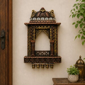 May include: A wall-mounted decorative frame featuring an arched opening, intricate carvings, and a domed top. The piece is finished in metallic bronze, gold, and silver tones with floral motifs, columns, and five small hanging pendants at the base.