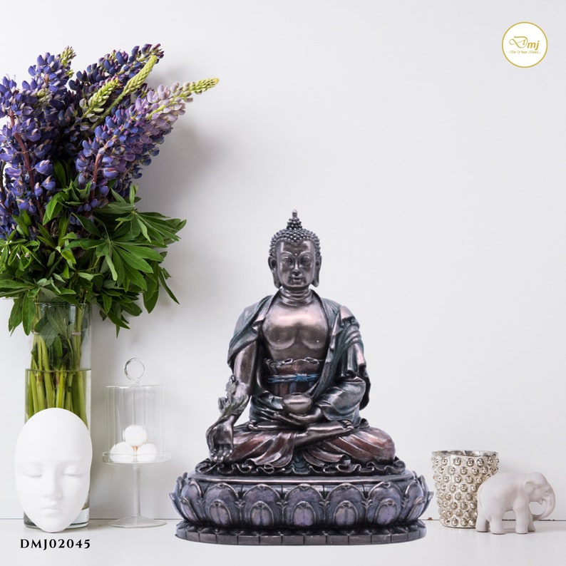 May include: A bronze-colored Buddha statue sitting in a meditative pose on a lotus flower base. The statue has a serene expression and is decorated with intricate details. The base is painted in shades of purple and blue.