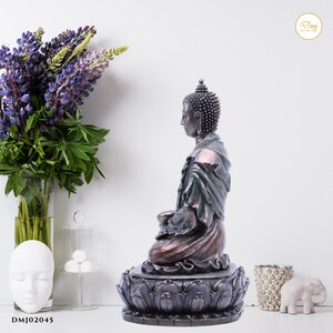 May include: A bronze-colored Buddha statue sitting in a meditative pose on a lotus base. The statue is detailed with a green robe and a serene expression.