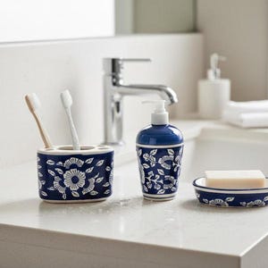 May include: A navy blue bathroom set with a white floral design, including a toothbrush holder, soap dish, and soap dispenser. The toothbrush holder has two toothbrushes. The soap dish holds a bar of soap.