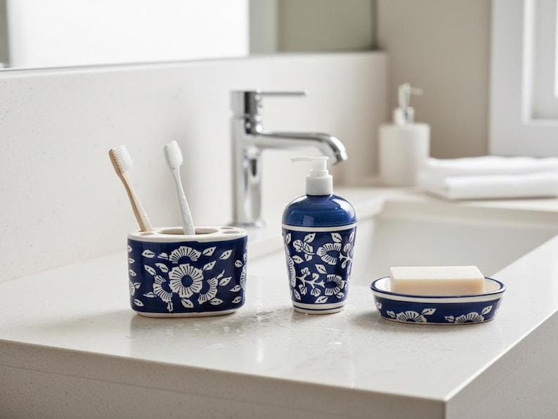 May include: A navy blue bathroom set with a white floral design, including a toothbrush holder, soap dish, and soap dispenser. The toothbrush holder has two toothbrushes. The soap dish holds a bar of soap.
