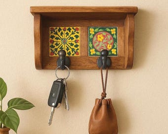 Puede incluir: Un llavero de madera con dos ganchos negros y baldosas decorativas. Las baldosas presentan motivos florales en amarillo, rojo y verde. Un juego de llaves cuelga de un gancho y una pequeña bolsa de cuero marrón del otro.