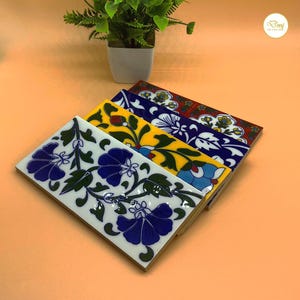 May include: A collection of rectangular ceramic tiles with floral patterns. The tiles display a range of colours, including white, blue, yellow, and red. Each tile showcases a distinct design of flowers and leaves, creating a decorative aesthetic.