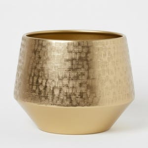 Puede incluir: Una maceta decorativa dorada con una mitad superior texturizada y una base lisa. La maceta tiene una abertura ancha y una forma geométrica cónica. El acabado metálico le da un aspecto moderno y elegante, adecuado para la decoración interior.
