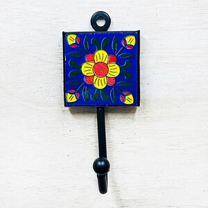 Könnte beinhalten: Ein schwarzer Metallhaken mit einem blauen und gelben Fliesenmuster mit Blumen. Die Fliese hat eine rote Mitte und gelbe Blütenblätter.