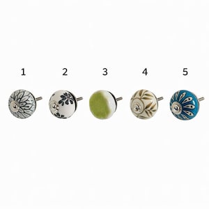 May include: Five decorative ceramic cabinet knobs. The knobs are round with metal stems. The knobs feature various designs, including floral patterns, leaf motifs, and a solid green knob. The knobs are in shades of white, blue, green, and brown.