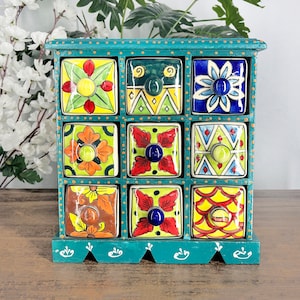May include: Teal wooden spice rack with 12 small drawers. Each drawer is decorated with a colorful floral design and has a knob.