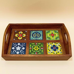 May include: A wooden serving tray with six colorful ceramic tiles featuring floral patterns. The tiles are arranged in a grid pattern and are set into the wooden frame. The tray has two handles on the sides.