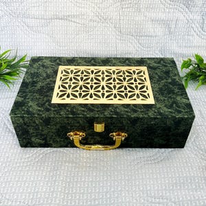 May include: A green gift box with a gold handle and a decorative gold lattice design on the lid.