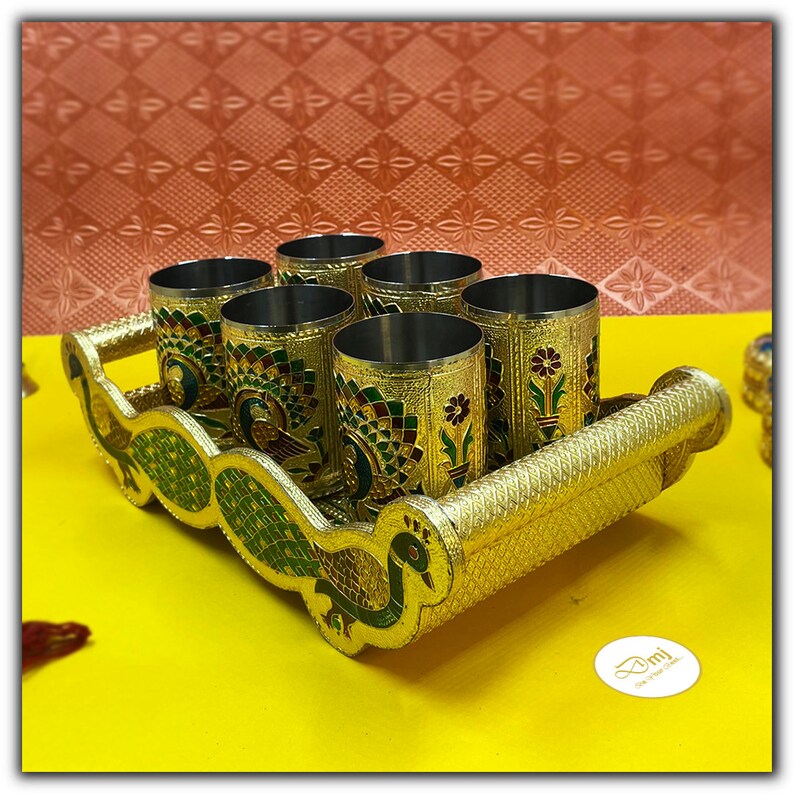 Puede incluir: Un juego de seis vasos de color dorado con dise&ntilde;os de pavo real, dispuestos en una bandeja dorada con dise&ntilde;os de pavo real. La bandeja tiene un asa en un lado.