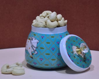 May include: A blue and white ceramic jar with a lid, featuring a cow design. The jar is filled with cashew nuts.