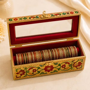 May include: A rectangular jewelry box with a hinged lid featuring a glass window and a gold metal latch. The exterior is decorated with painted red and green floral patterns on a gold background. The interior is lined with red velvet.