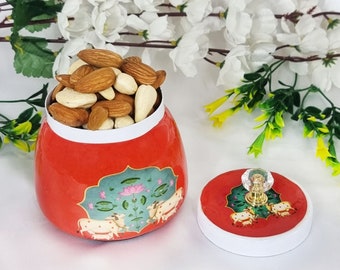 May include: Red and white ceramic jar with a floral design and a crystal knob lid. The jar is filled with almonds and cashews.