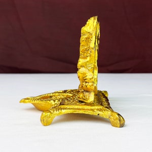 May include: A gold-colored metal stand with an ornate design. The stand has a round top and three legs. The stand is made of metal and has a gold finish.