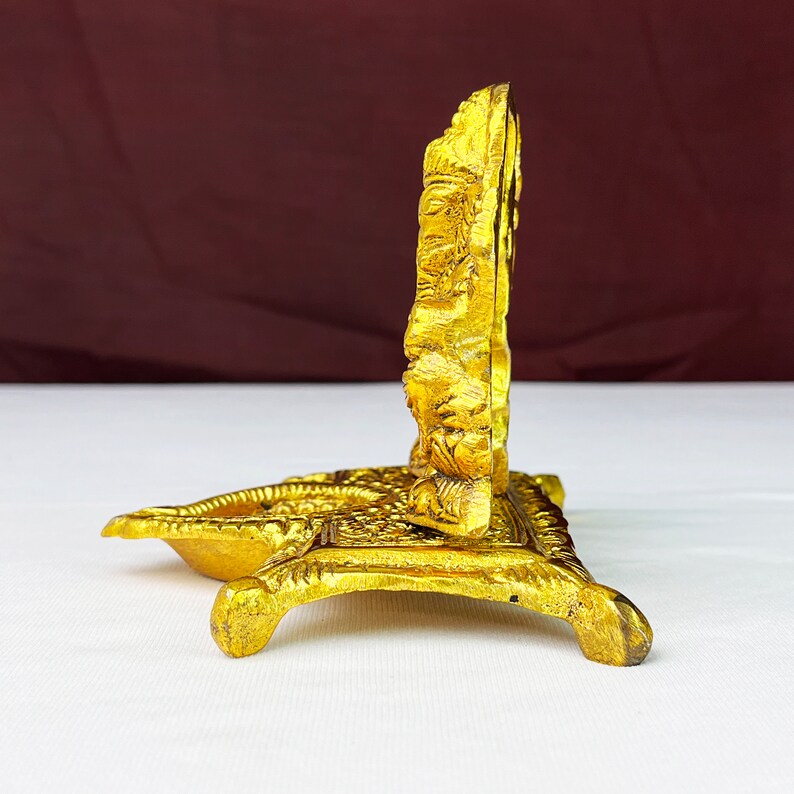 May include: A gold-colored metal stand with an ornate design. The stand has a round top and three legs. The stand is made of metal and has a gold finish.