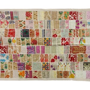 Puede incluir: Un edredón rectangular de patchwork con un borde color crema. El edredón está compuesto por numerosos cuadrados de tela en varios colores y patrones, incluyendo diseños florales, paisley y geométricos. El edredón tiene borlas en las esquinas.