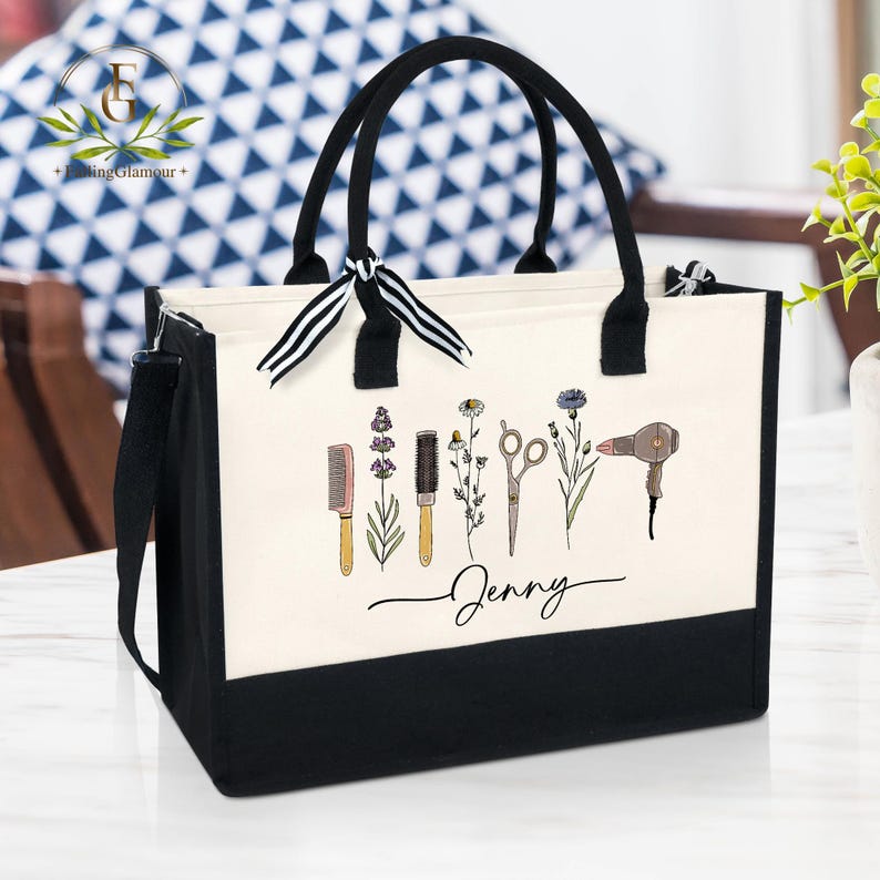 May include: A black and white tote bag with black handles and a black shoulder strap. The bag features a cream-colored front panel with illustrations of salon tools and flowers, along with the name "Jenny" in script.