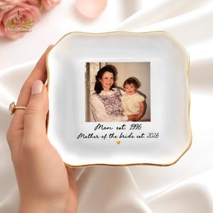 May include: White ceramic trinket dish with a gold rim, featuring a vintage photograph of a mother and child. The dish is inscribed with "Mom est. 1996" and "Mother of the bride est. 2026". A thoughtful gift.