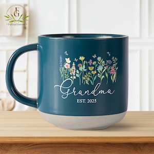 May include: Teal blue ceramic mug with a white and grey base. The mug features a floral design with butterflies and the text "Grandma Est. 2025".