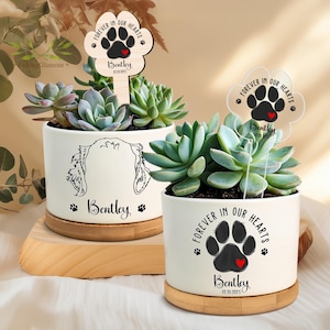 May include: Two white ceramic planters with bamboo bases, each with a succulent plant and a wooden stake. The stakes have a black paw print with a red heart and the text "Forever in our hearts" with the name "Bentley" and a date.