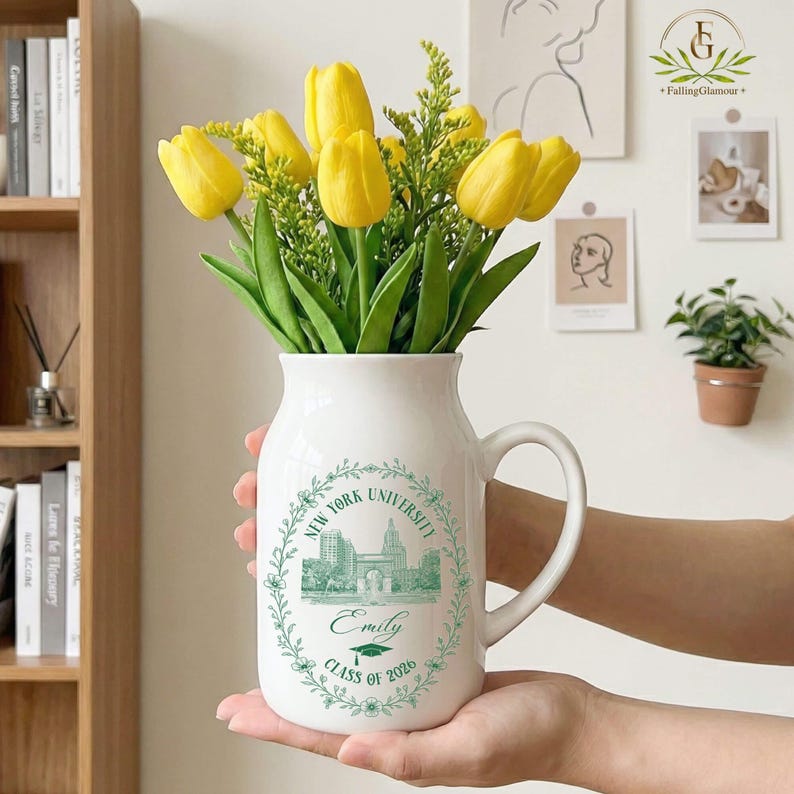 Pu&ograve; includere: Un vaso di ceramica bianca con manico, pieno di tulipani gialli e verde. Il vaso &egrave; decorato con un disegno verde con il testo "New York University", il nome "Emily" e "Class of 2026".