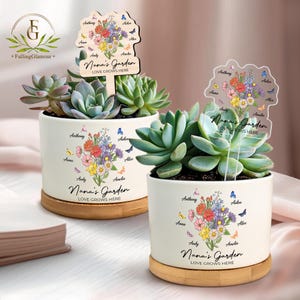 May include: Two white ceramic succulent planters with bamboo saucers. Each planter features a floral design, butterflies, and the text "Nana's Garden LOVE GROWS HERE." One planter has a wooden sign, the other a clear acrylic sign.