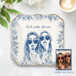 May include: A white decorative plate with a blue floral border and gold trim. The plate features a blue illustration of two women wearing heart-shaped sunglasses and licking lollipops, with the text "Soul sister forever". A small photo is in the bottom right corner.