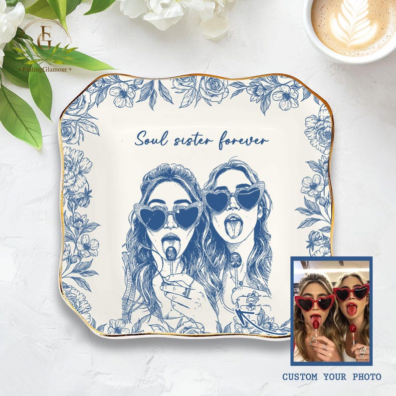 May include: A white decorative plate with a blue floral border and gold trim. The plate features a blue illustration of two women wearing heart-shaped sunglasses and licking lollipops, with the text "Soul sister forever". A small photo is in the bottom right corner.