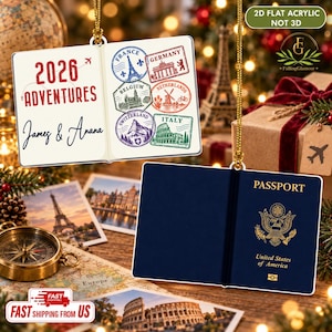 May include: A flat 2D acrylic ornament shaped like an open passport. One side shows the text 2026 ADVENTURES with names James & Anana and colorful travel stamps. The other side is a dark blue United States of America passport cover.