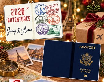 May include: A flat 2D acrylic ornament shaped like an open passport. One side shows the text 2026 ADVENTURES with names James & Anana and colorful travel stamps. The other side is a dark blue United States of America passport cover.