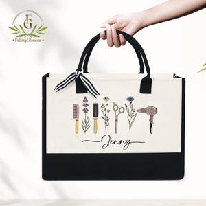 May include: A black and white tote bag with black handles and a black bottom. The bag features a cream-colored front panel with illustrations of hair styling tools and flowers. The name "Jenny" is written in cursive below the illustrations.