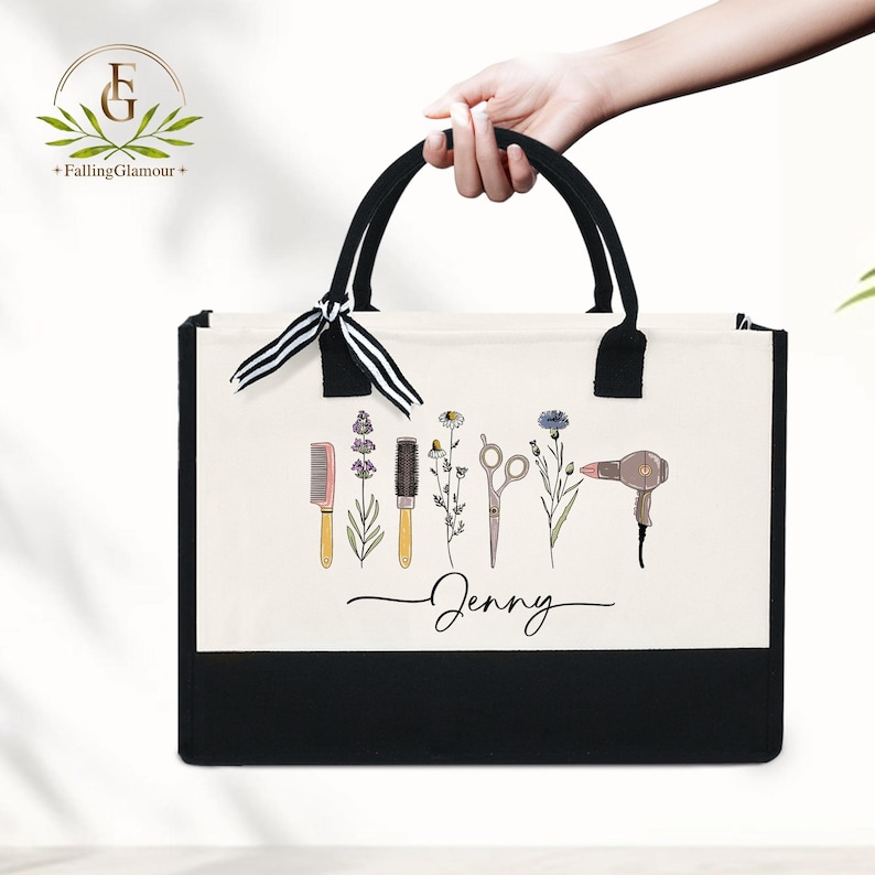 May include: A black and white tote bag with black handles and a black bottom. The bag features a cream-colored front panel with illustrations of hair styling tools and flowers. The name "Jenny" is written in cursive below the illustrations.
