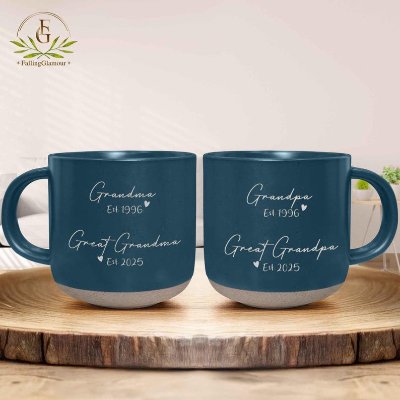 May include: Two blue ceramic mugs with white text. The mug on the left says "Grandma Est 1996 Great Grandma Est 2025". The mug on the right says "Grandpa Est 1996 Great Grandpa Est 2025".