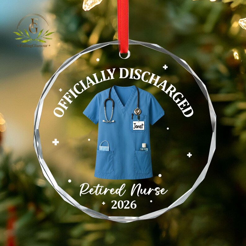 K&ouml;nnte beinhalten: Ein klarer, runder Weihnachtsschmuck mit den Worten "OFFICIALLY DISCHARGED" und "Retired Nurse 2026" in Wei&szlig;. Der Schmuck zeigt einen blauen medizinischen Kittel mit Stethoskop, Gesichtsmaske und H&auml;ndedesinfektionsmittel. Ein rotes Band ist zum Aufh&auml;ngen befestigt.