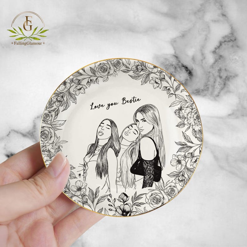May include: A white ceramic plate with a gold rim, featuring a black and white illustration of three women and floral border. The text "Love you Bestie" is written on the plate.