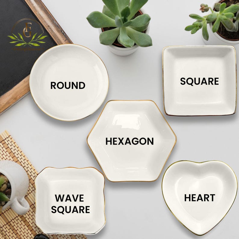 May include: A collection of white ceramic dishes in various shapes: round, square, hexagon, wave square, and heart. Each dish has a gold trim and a black label indicating its shape. The dishes are arranged on a white surface.