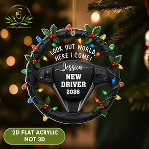 May include: A flat acrylic hanging ornament shaped like a black steering wheel, decorated with green holly leaves, red berries, and colorful Christmas lights. The text reads: LOOK OUT WORLD, HERE I COME! Jessica NEW DRIVER 2026.
