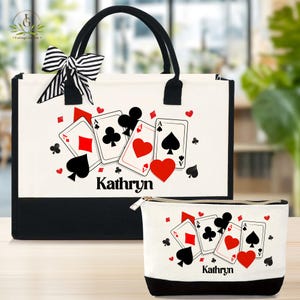 May include: A canvas tote bag and matching zippered pouch, both featuring a playing card design with the name "Kathryn". The tote has black handles and a black and white striped bow. The design includes red hearts, black spades, clubs, and diamonds.