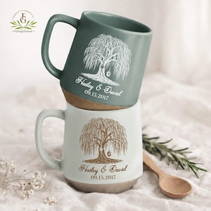 May include: Two ceramic mugs stacked vertically. The top mug is sage green with a white willow tree illustration, the names Hailey & David, and the date 09.15.2017. The bottom mug is off-white with a brown willow tree, names, and date.