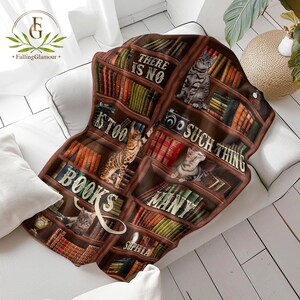 May include: A brown and white throw blanket with a bookshelf design featuring cats and books. The text on the blanket reads "There is no such thing as too many books".