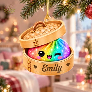 May include: A hanging Christmas ornament shaped like a bamboo steamer basket containing a rainbow-colored, glittery dumpling with a cute, winking face. The wooden steamer base is personalized with the name Emily and two small heart icons.