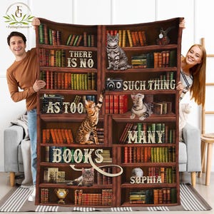 May include: A brown wooden bookshelf with multiple shelves filled with books. The shelves are decorated with cats, a typewriter, and a camera. The text "There is no such thing as too many books" is written on the bookshelf. The name "Sophia" is written on the bottom shelf.