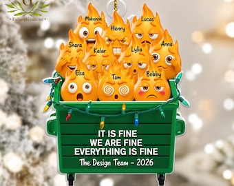 May include: A green dumpster ornament decorated with string lights, filled with orange flame characters featuring various facial expressions and names. The text reads: IT IS FINE WE ARE FINE EVERYTHING IS FINE The Design Team - 2026.